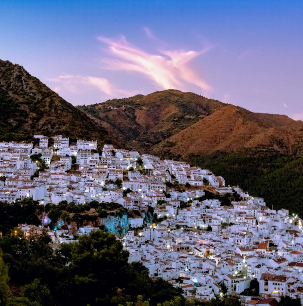 Un pueblo blanco en la ladera al anochecer, bajo las montañas